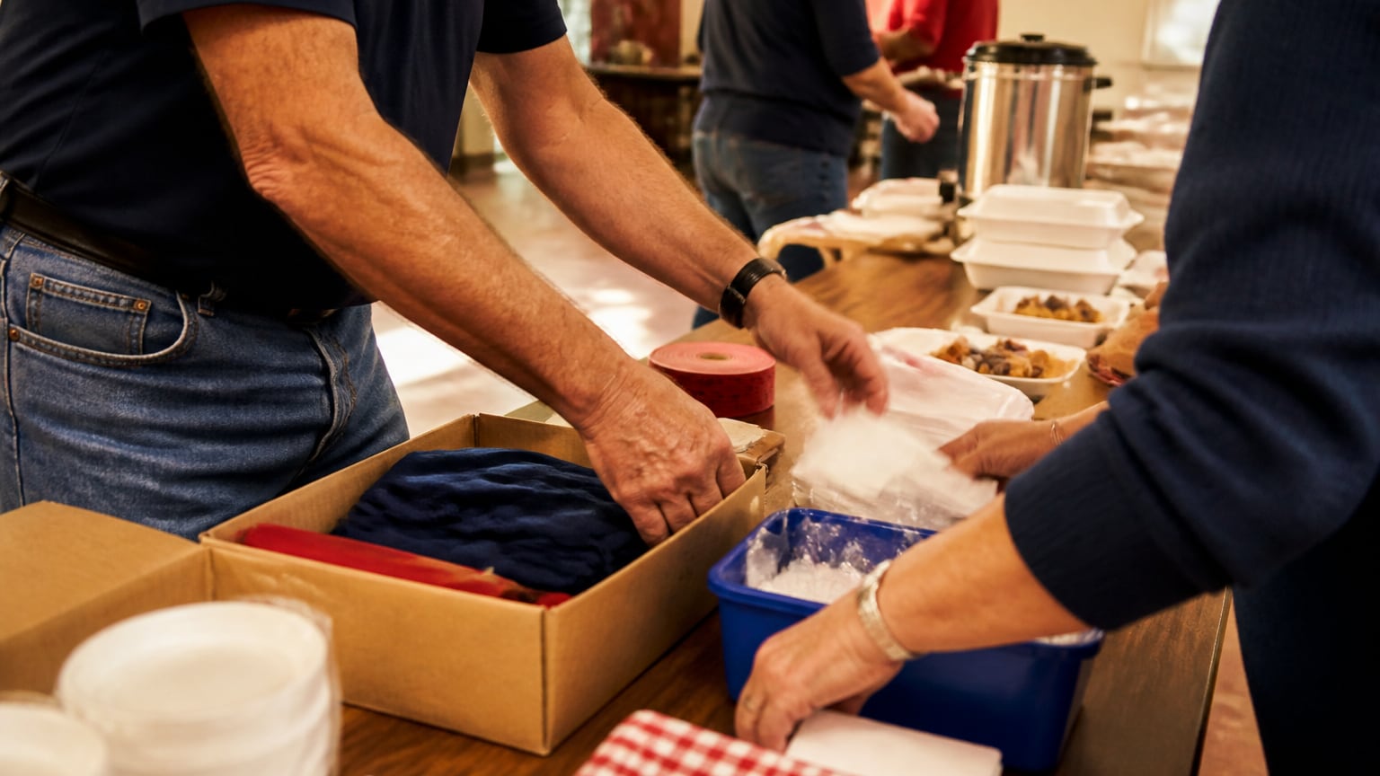 Volunteers' hands organizing supplies and meal trays at a community support event.